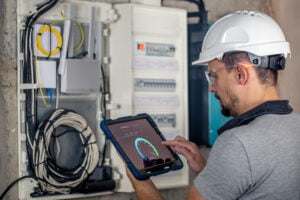 Empowering Real-Time Power Management with Smart Metering Man, an electrical technician working in a switchboard with fuses, uses a tablet.